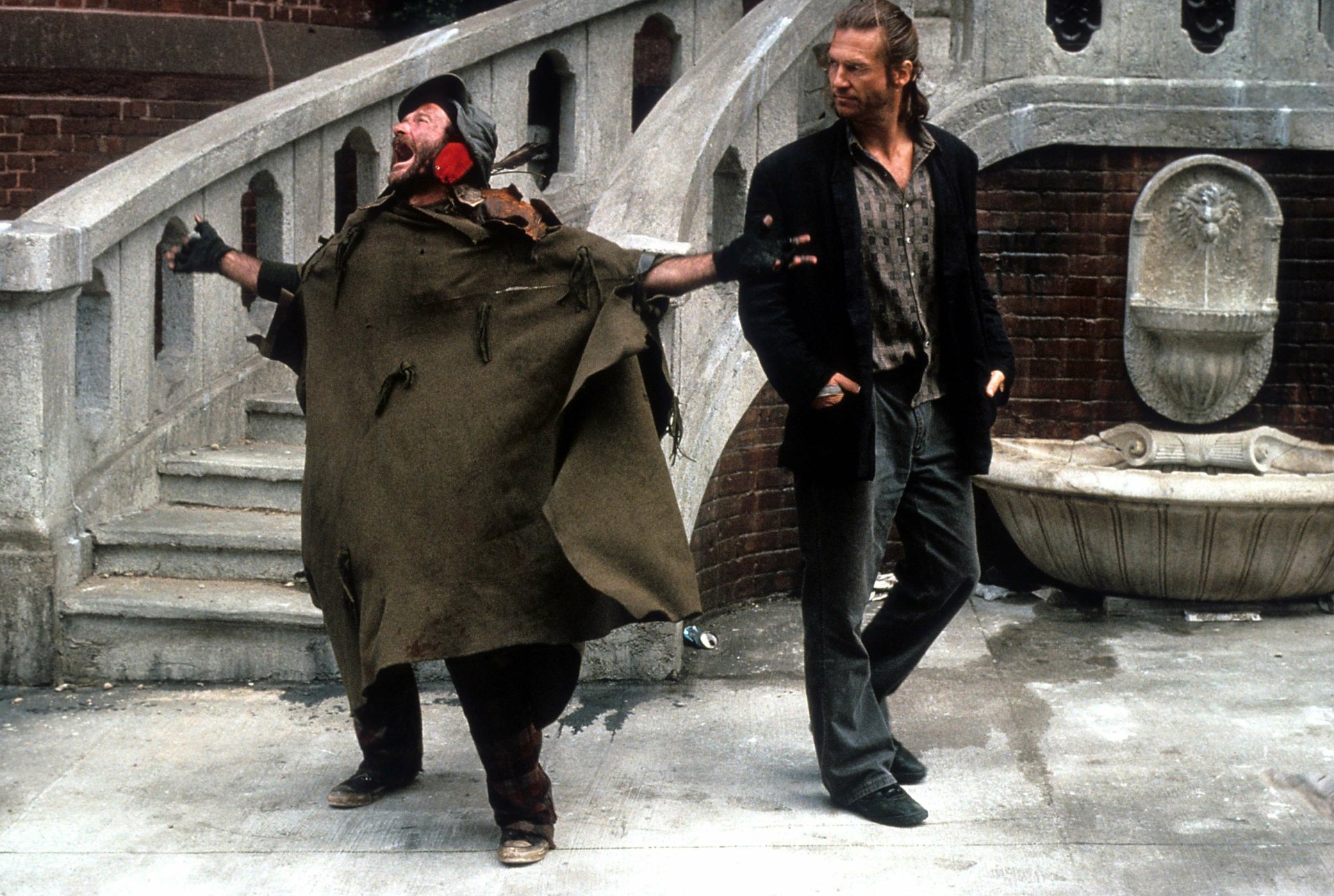 HD wallpaper featuring a scene from The Fisher King with two characters walking in front of an urban fountain.