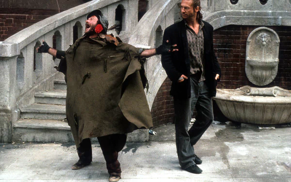 HD wallpaper featuring a scene from The Fisher King with two characters walking in front of an urban fountain.