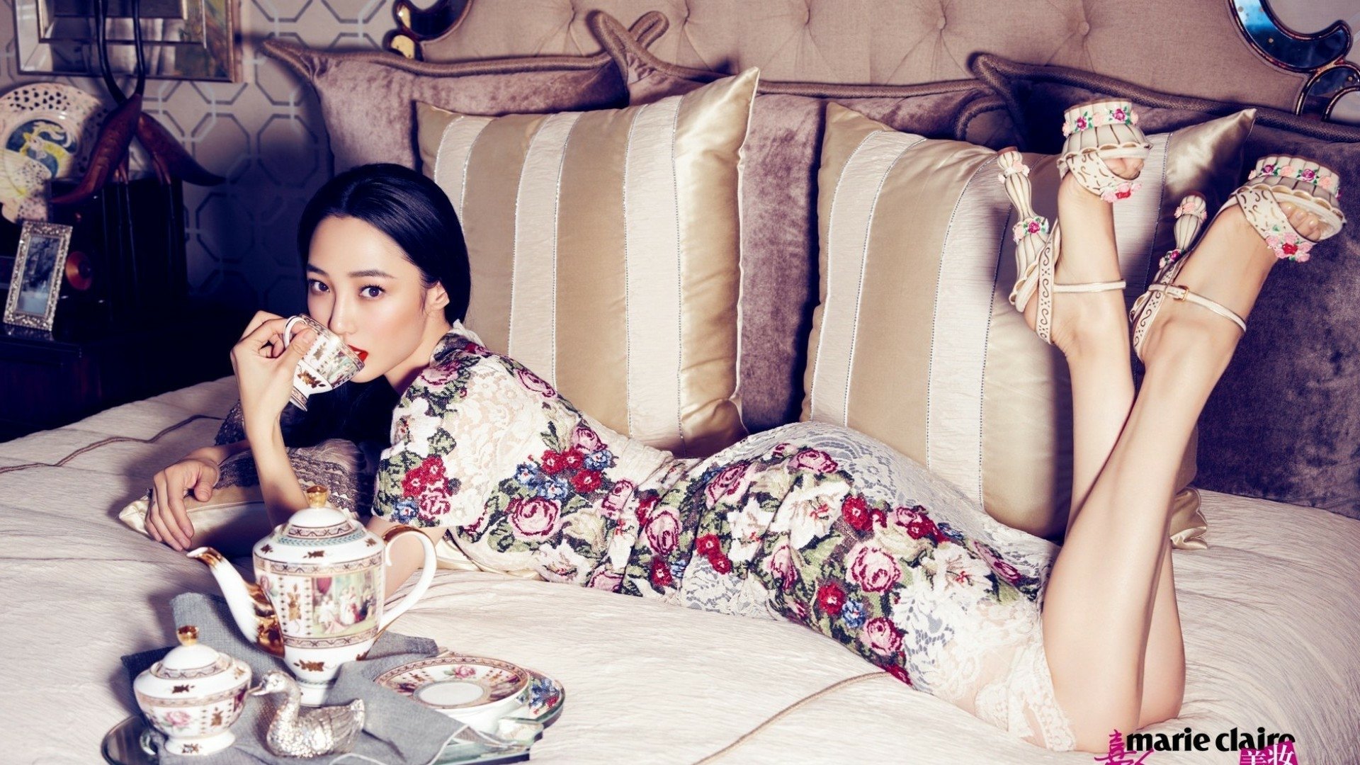 HD PC desktop wallpaper featuring actress Baihe Bai reclining on a sofa, dressed in a floral outfit, sipping tea from a delicate cup in an elegant setting.