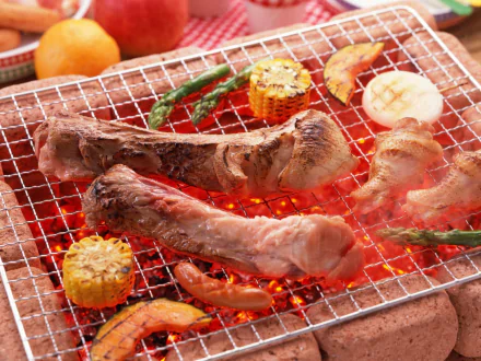 HD desktop wallpaper showing a barbecue meal with grilled pork, chicken, corn, and vegetables over glowing coals.