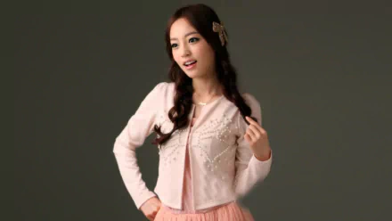 HD Korean K-pop music desktop wallpaper showing a female idol in a pink dress and cardigan, posing against a neutral gray background.