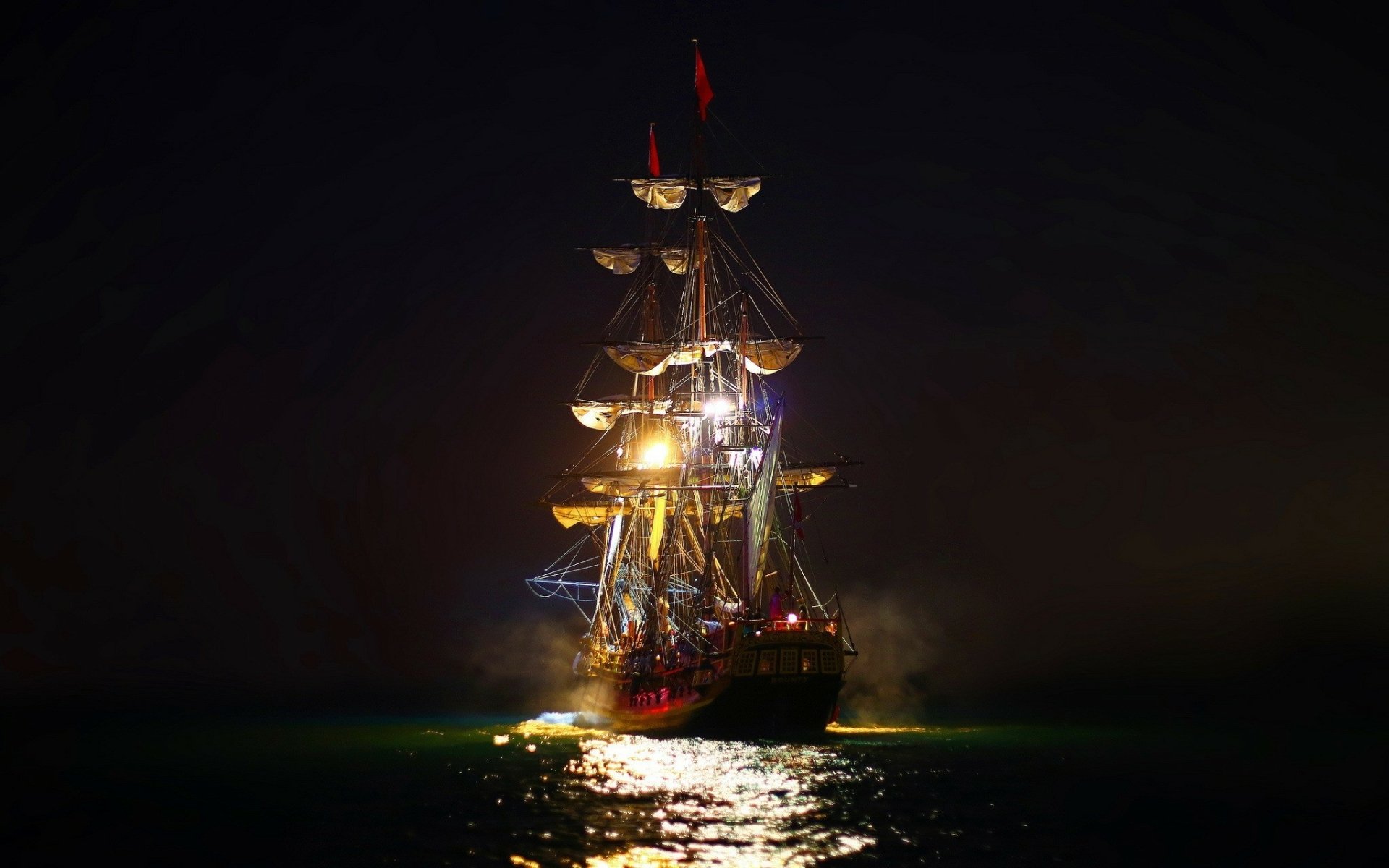 HD desktop wallpaper featuring a sailboat illuminated against a dark night background, highlighting its intricate rigging and reflecting on the water's surface.