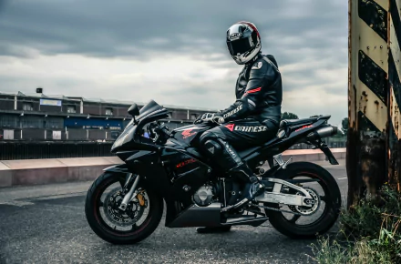 2K Quad HD PC desktop wallpaper showing a Honda sport motorcycle (vehicle) with a rider in black racing leathers and helmet parked on an urban road under a moody cloudy sky.