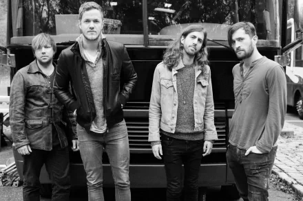 A black and white image of the band Imagine Dragons posing in front of a tour bus, showcasing their style and camaraderie. This serves as a striking HD wallpaper for music fans.