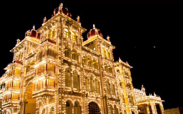 Mysore Palace illuminated at night, showcasing its grand architecture in Karnataka, India. A stunning HD desktop wallpaper capturing the beauty of this man-made landmark.