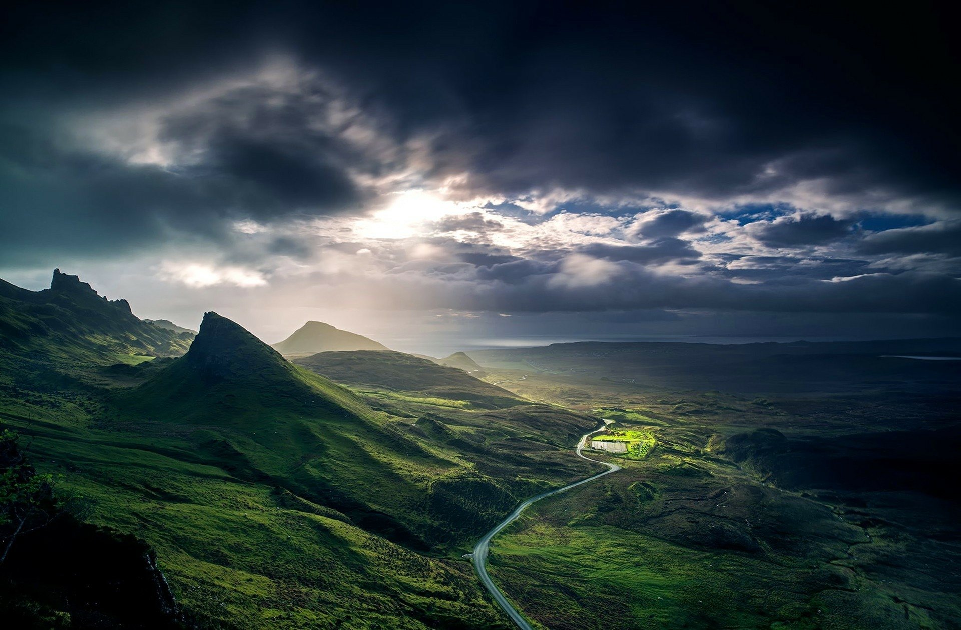 A winding road meanders through a lush green landscape under dramatic skies, capturing the essence of nature's beauty in a striking HD desktop wallpaper.
