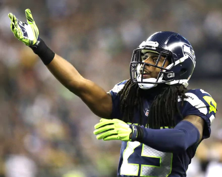 A dynamic Seattle Seahawks player with dreadlocks gestures energetically on the field, captured in an HD desktop wallpaper showcasing the excitement of sports.