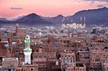 A stunning HD view of Sana'a, Yemen, showcasing the minaret of Al Saleh Mosque against a backdrop of traditional architecture and majestic mountains at sunset.