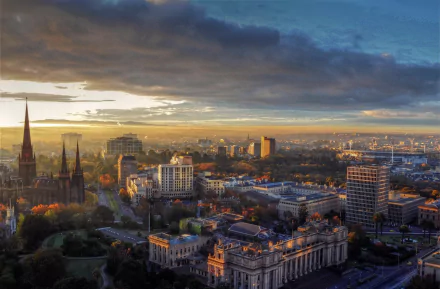 A stunning aerial view of Melbourne, Australia, showcasing the cityscape illuminated by sunlight, with iconic church spires contrasting against the modern skyline. HD desktop wallpaper.