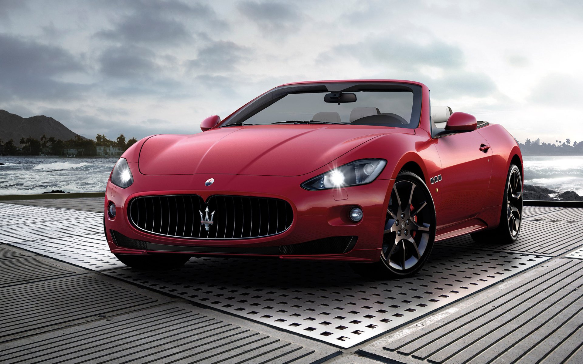 HD PC desktop wallpaper of a red Maserati convertible parked on a dock by the water under a cloudy sky.