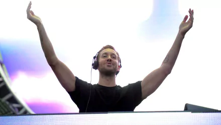 Calvin Harris performing live, raising his arms in excitement, with vibrant lighting in the background; an engaging HD desktop wallpaper for music fans.
