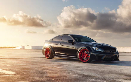 Black Mercedes-Benz C63 coupe with red rims on a sunlit waterfront at golden hour — 2K Quad HD PC desktop wallpaper/background showing the Mercedes-Benz vehicle.