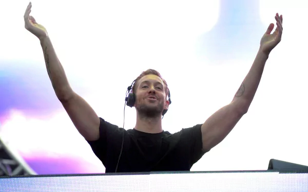 Calvin Harris performing live, raising his arms in excitement, with vibrant lighting in the background; an engaging HD desktop wallpaper for music fans.