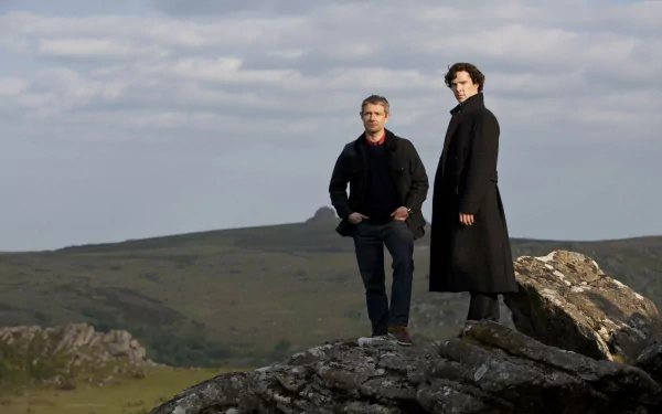 Dr. Watson and Sherlock Holmes stand on a rocky outcrop against a scenic backdrop, captured in this HD wallpaper from the acclaimed TV series Sherlock featuring Martin Freeman and Benedict Cumberbatch.
