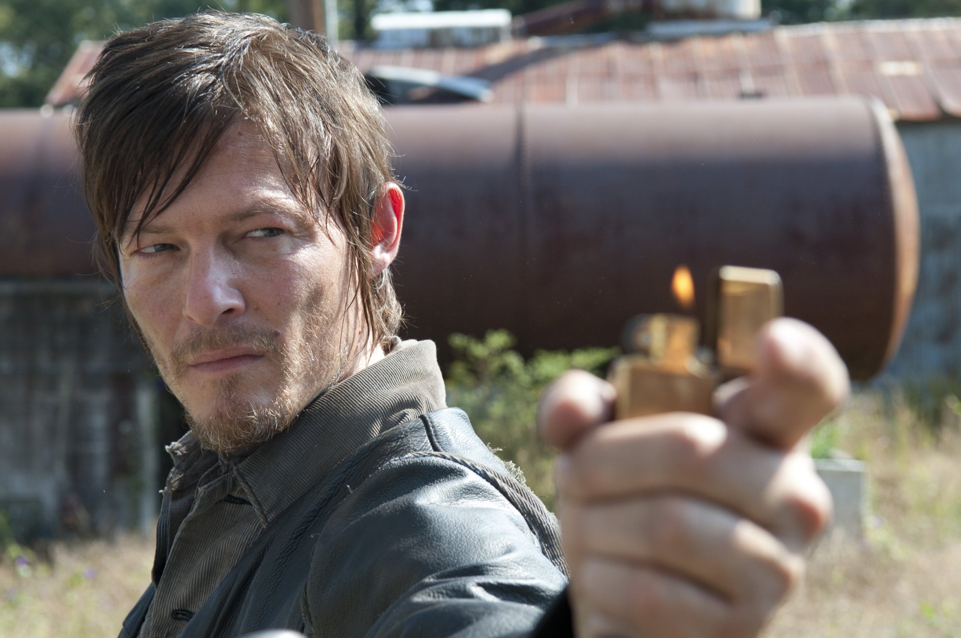 HD PC desktop wallpaper featuring a close-up of a character from The Walking Dead TV show holding a lighter against an industrial background.