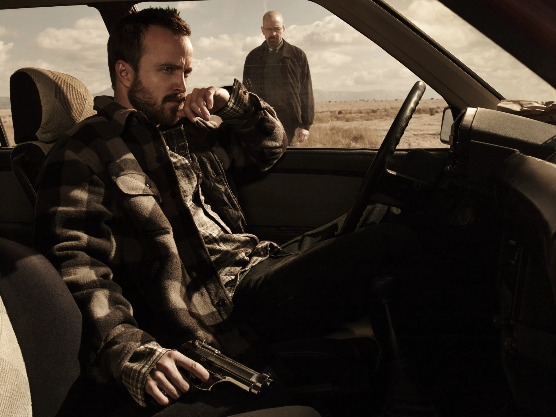 2K Quad HD Breaking Bad desktop wallpaper: tense desert scene with a man seated in a car holding a gun and another standing nearby, gritty cinematic lighting.