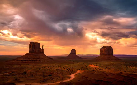 A dramatic sunset over Monument Valley's desert landscape with towering rock formations beneath a vibrant, cloudy sky, captured in HD for a PC desktop wallpaper.