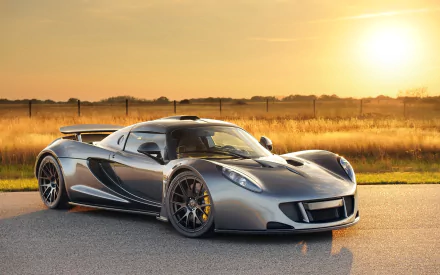A stunning HD desktop wallpaper featuring a sleek silver Hennessey Venom GT supercar, parked on a road with a golden sunset in the background.