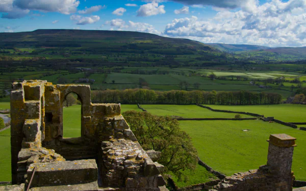 HD PC desktop wallpaper: Bolton Castle's man-made ruins on a hill overlooking patchwork green fields and distant hills under a blue sky.