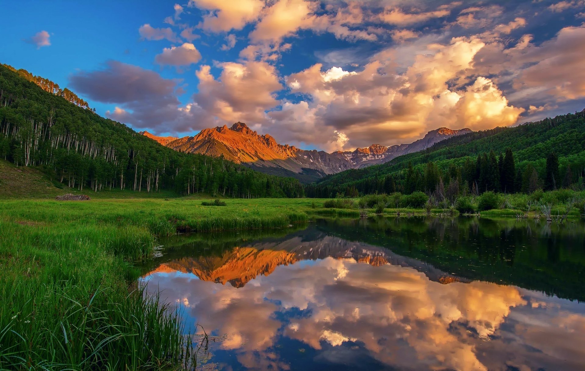 HD desktop wallpaper showcasing a vibrant mountain landscape with clouds reflected in a calm lake, surrounded by lush green nature.