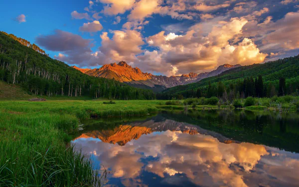 HD desktop wallpaper showcasing a vibrant mountain landscape with clouds reflected in a calm lake, surrounded by lush green nature.
