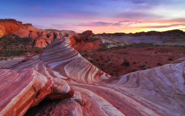 HD PC desktop wallpaper/background: sunset over a striped sandstone canyon, sweeping wave-like rock formations and rich red and purple hues beneath a glowing, multicolored sky.