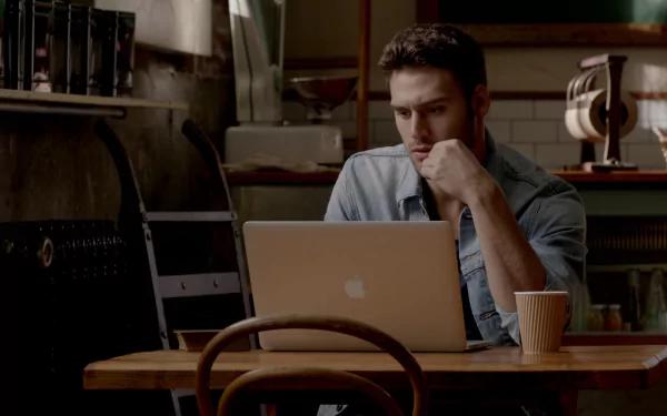 Ryan Guzman in a scene from *Step Up All In*, focused while working on a laptop at a wooden table, with a coffee cup nearby, set in a cozy café environment.