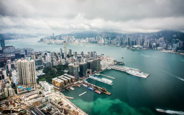 A 4K Ultra HD aerial view of Hong Kong’s man-made skyline, featuring dense skyscrapers and busy harbor waters under a cloudy sky.