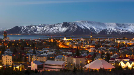4K Ultra HD cityscape of Reykjavik, Iceland at dusk, showcasing illuminated buildings with snow-capped mountains in the background.
