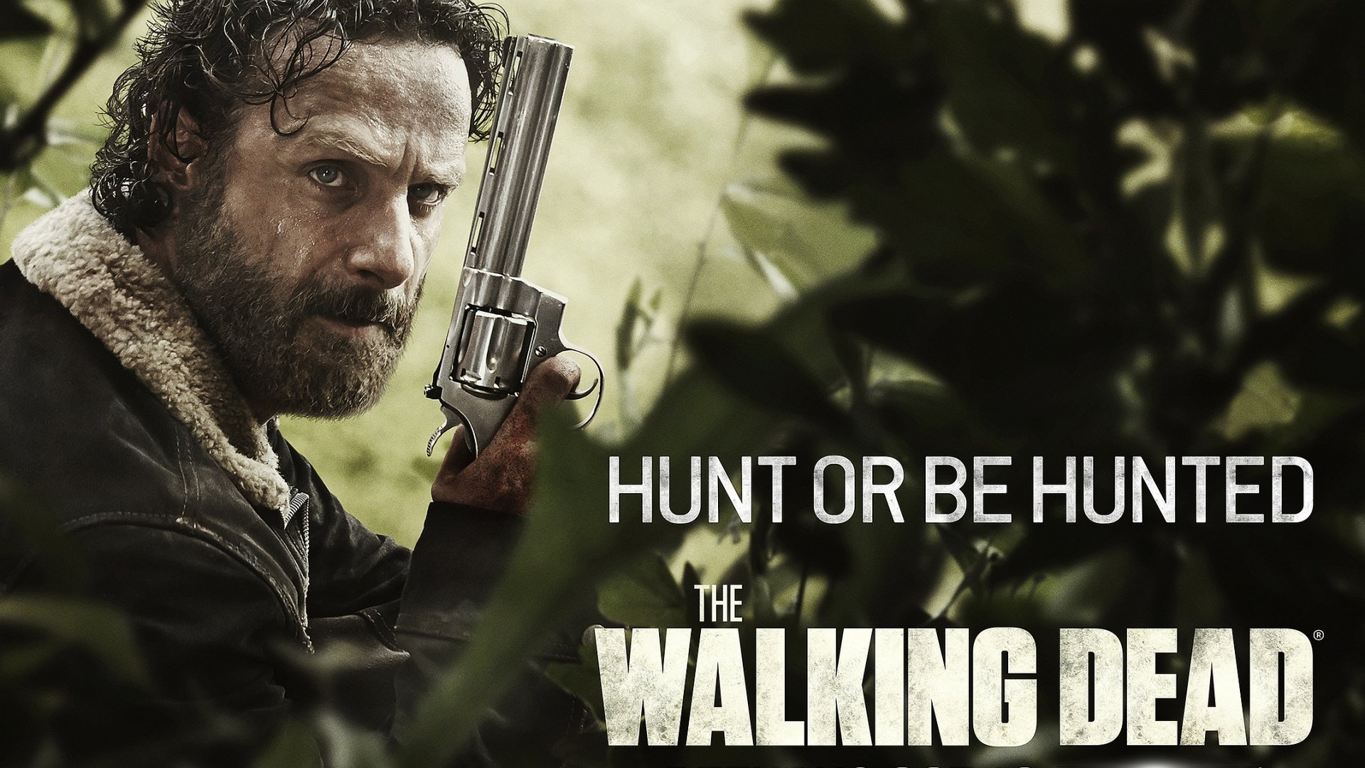 HD desktop wallpaper featuring Andrew Lincoln as Rick Grimes from *The Walking Dead*, showcasing him with a gun in a tense, survival-themed scene. The tagline reads Hunt or be hunted.