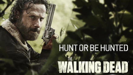 HD desktop wallpaper featuring Andrew Lincoln as Rick Grimes from *The Walking Dead*, showcasing him with a gun in a tense, survival-themed scene. The tagline reads Hunt or be hunted.