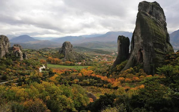 A magical mountain landscape features towering rock formations amidst a vibrant, autumnal valley, capturing the enchanting beauty of nature in stunning HD detail.