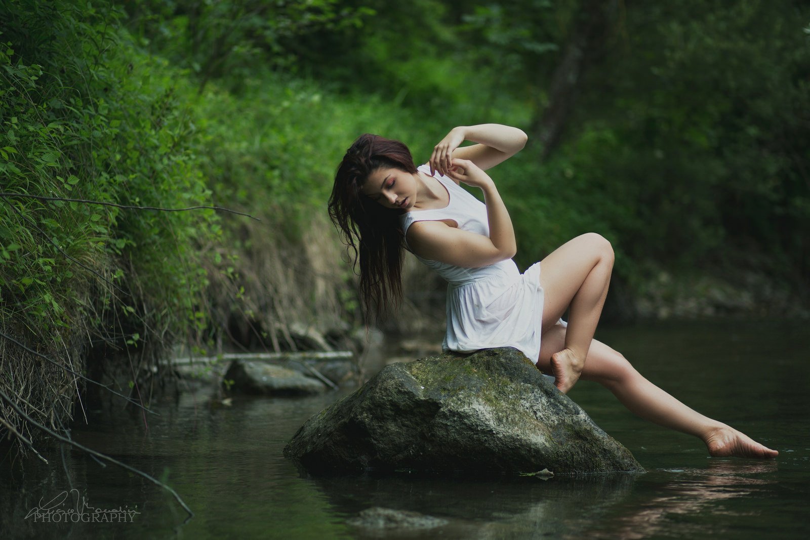 Artistic HD desktop wallpaper featuring a woman in a white dress, gracefully posed on a rock in a tranquil forest stream setting.