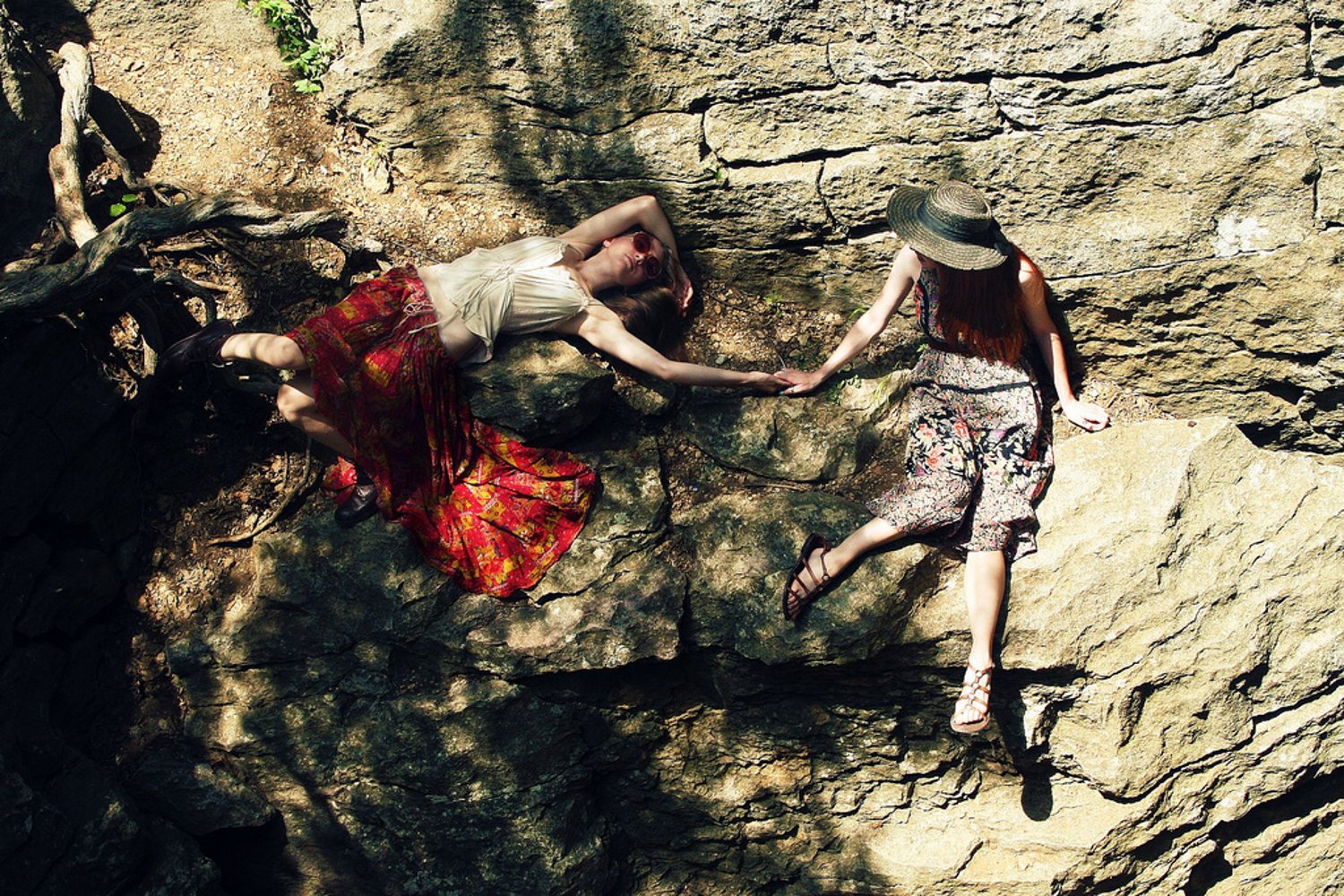 HD PC desktop wallpaper featuring two women in floral skirts holding hands against a rocky background, symbolizing connection and love.
