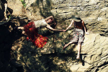 HD PC desktop wallpaper featuring two women in floral skirts holding hands against a rocky background, symbolizing connection and love.