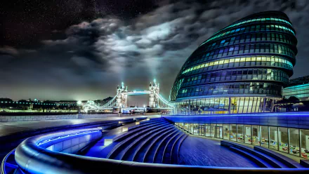 A stunning view of Tower Bridge illuminated at night, framed by the modern architecture of City Hall, showcasing London's vibrant cityscape in 4K Ultra HD.