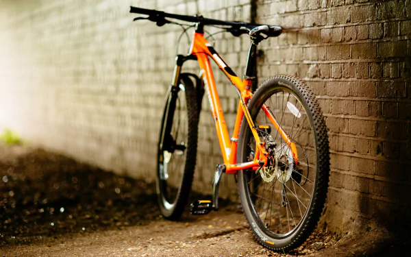 HD desktop wallpaper featuring an orange bicycle leaning against a brick wall, showcasing a dynamic blend of urban exploration and sporty style.