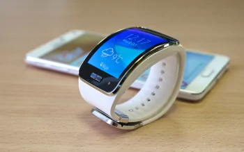 Samsung Galaxy smartwatch with two Galaxy phones on a wooden desk — technology-themed 4K Ultra HD PC desktop wallpaper.