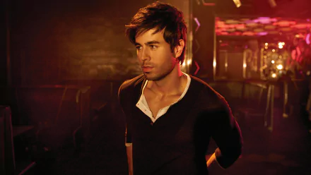 A striking HD desktop wallpaper featuring Enrique Iglesias, captured in a dimly lit setting, exuding charisma and style against a vibrant, colorful backdrop.