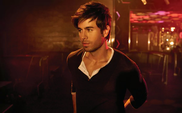 A striking HD desktop wallpaper featuring Enrique Iglesias, captured in a dimly lit setting, exuding charisma and style against a vibrant, colorful backdrop.