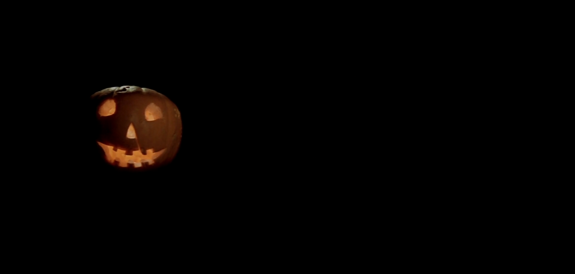 HD Halloween holiday desktop wallpaper featuring a glowing carved pumpkin with a spooky smile on a black background.
