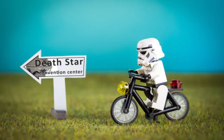 HD PC desktop wallpaper featuring a man-made LEGO stormtrooper riding a bicycle beside a sign pointing to the Death Star convention center.