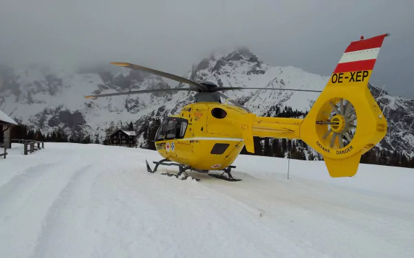 A bright yellow military helicopter sits on a snowy landscape, surrounded by majestic mountains. This HD image serves as an impressive desktop wallpaper or background.