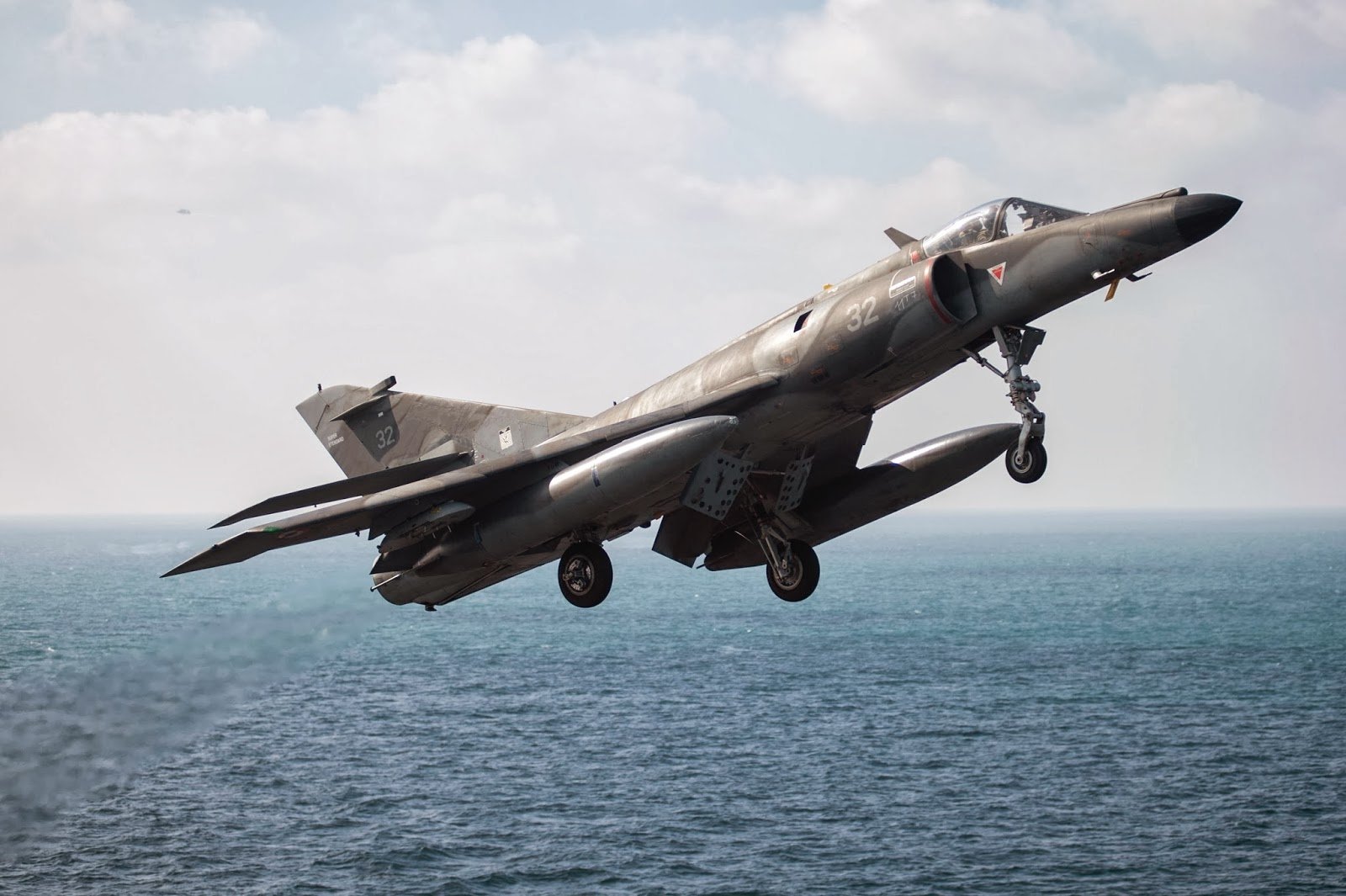 HD PC desktop wallpaper of a Dassault-Breguet Super Étendard jet fighter — a military air force aircraft in flight over the ocean with landing gear down.