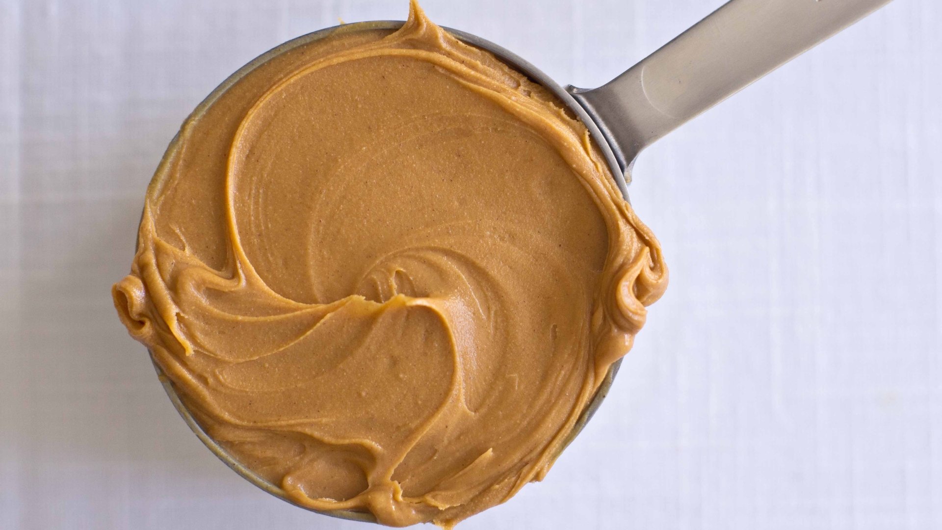 Close-up of smooth peanut butter swirled on a spoon — food-themed 4K Ultra HD PC desktop wallpaper background with rich golden-brown texture.