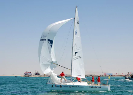 Sailors competing in the World Military Sailing Championship navigate a sailboat on clear blue waters, representing navy military sports with full sails against a calm sky.
