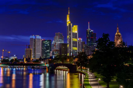 Night view of Frankfurt’s skyline in Germany showcasing illuminated skyscrapers and a man-made bridge reflected on the calm river in 4K Ultra HD quality.