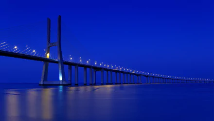 HD desktop wallpaper featuring the illuminated Vasco da Gama Bridge stretching over calm waters against a deep blue evening sky.