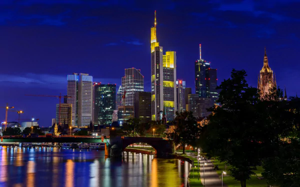 Night view of Frankfurt’s skyline in Germany showcasing illuminated skyscrapers and a man-made bridge reflected on the calm river in 4K Ultra HD quality.