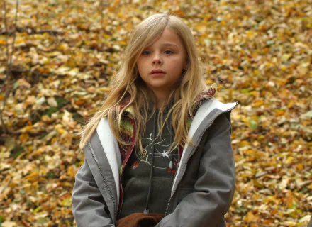 A high-definition desktop wallpaper featuring a young Chloë Grace Moretz, standing outdoors amidst a backdrop of autumn leaves.